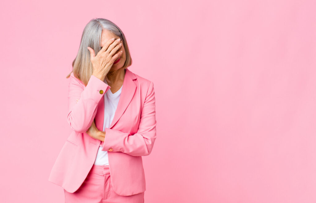 middle age cool woman looking stressed, ashamed or upset, with a headache, covering face with hand against flat wall