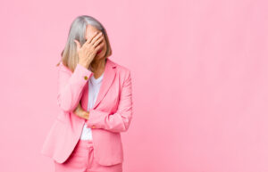 middle age cool woman looking stressed, ashamed or upset, with a headache, covering face with hand against flat wall