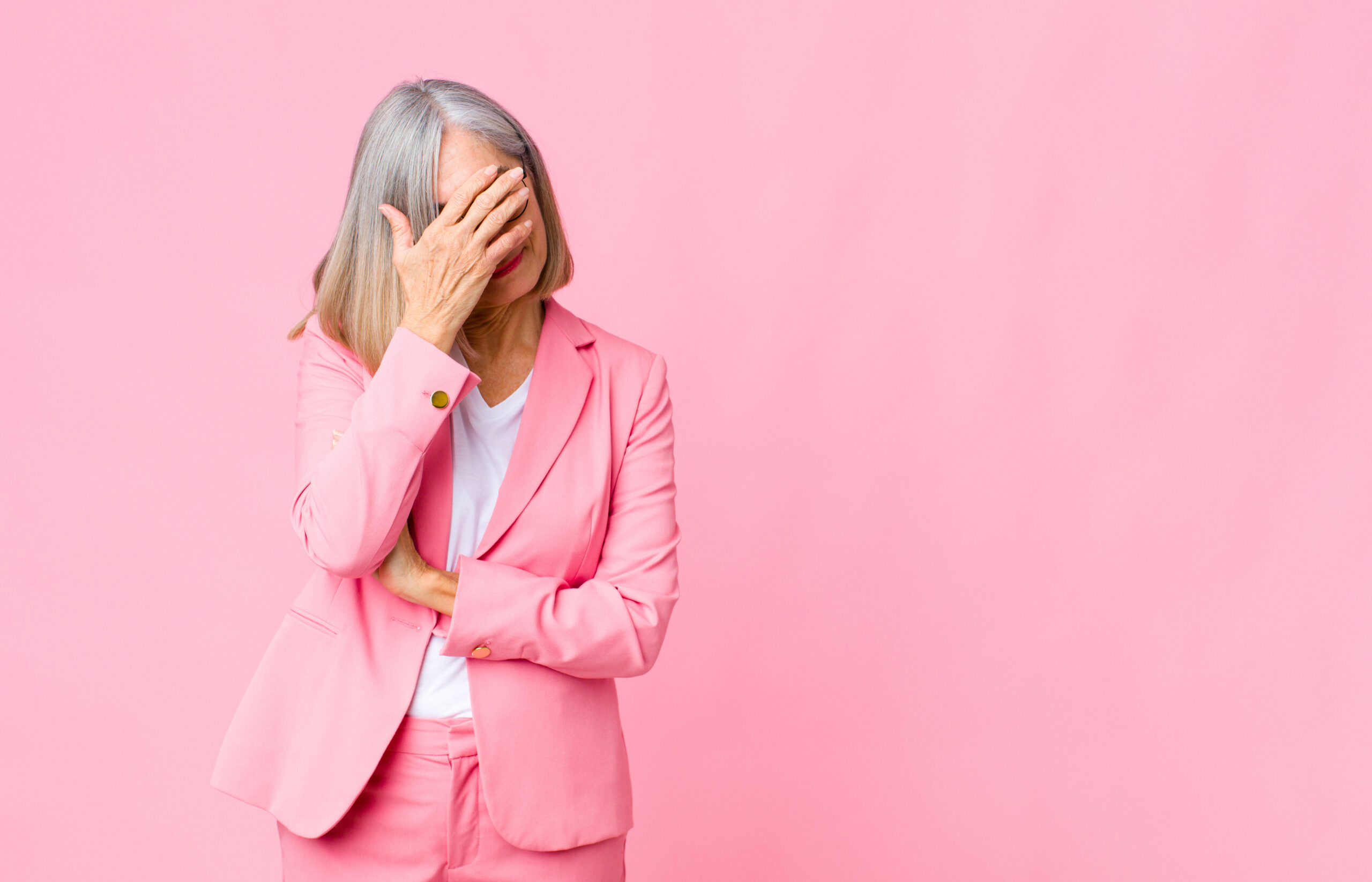 middle age cool woman looking stressed, ashamed or upset, with a headache, covering face with hand against flat wall