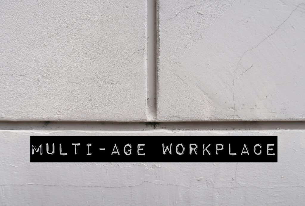 White office wall with words MULTI-AGE WORKPLACE, refers to multi-generational workforce and age diversity in environment in office or organization