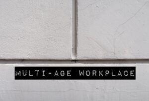 White office wall with words MULTI-AGE WORKPLACE, refers to multi-generational workforce and age diversity in environment in office or organization
