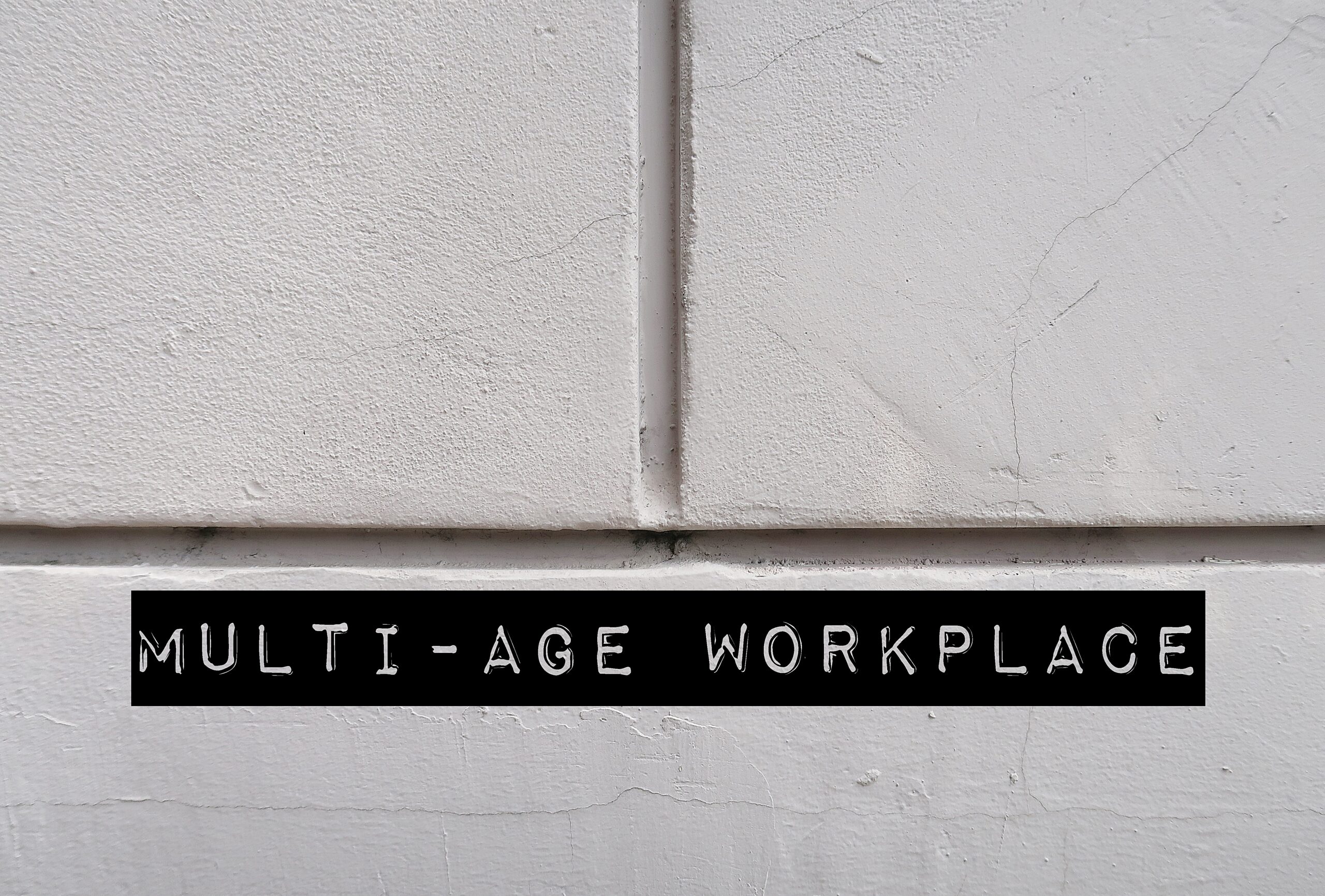 White office wall with words MULTI-AGE WORKPLACE, refers to multi-generational workforce and age diversity in environment in office or organization
