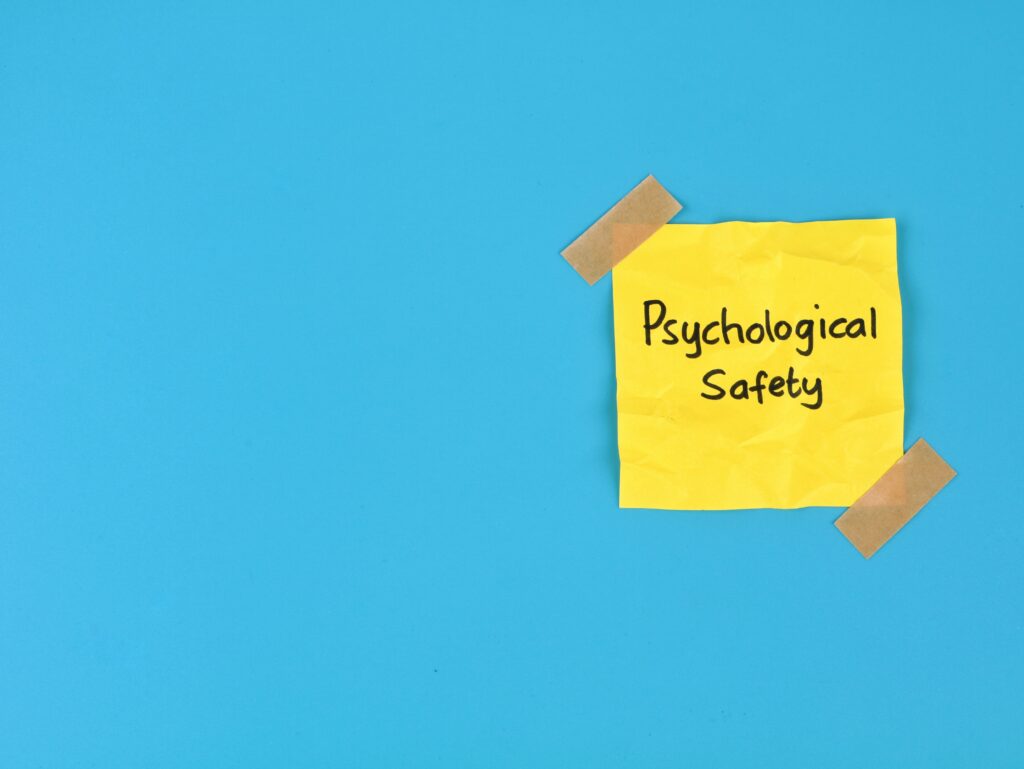 Psychological safety text handwritten on yellow adhesive note over blue background. Perfect for business management, positive workplace culture, mental health, teamwork, and employee well-being