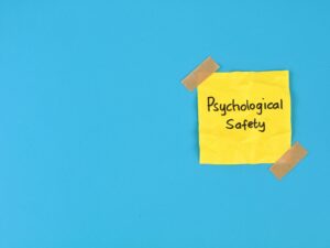 Psychological safety text handwritten on yellow adhesive note over blue background. Perfect for business management, positive workplace culture, mental health, teamwork, and employee well-being