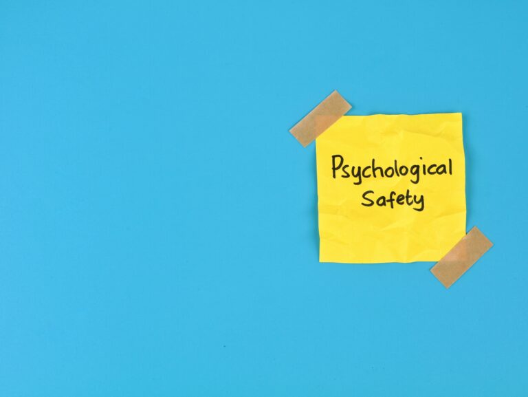 Psychological safety text handwritten on yellow adhesive note over blue background. Perfect for business management, positive workplace culture, mental health, teamwork, and employee well-being